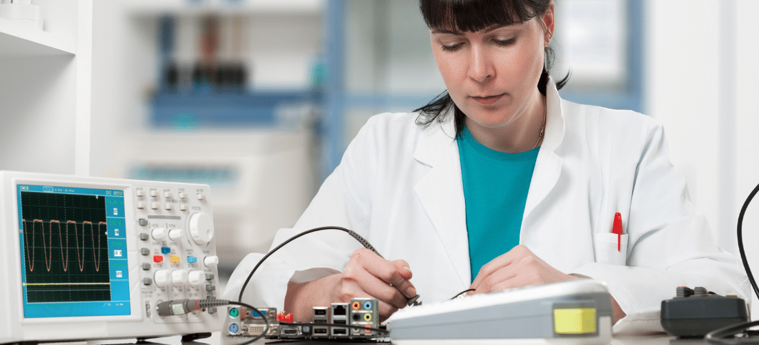 Technician probing a circuit board while a digital oscilloscope beside her shows a repeating pulse waveform