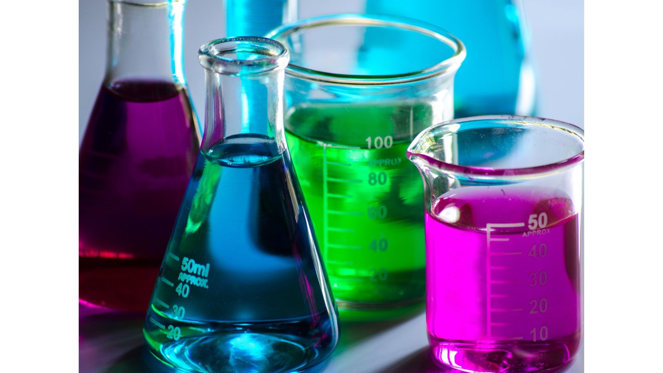 Glass conical flasks and graduated beakers holding purple, blue, and green liquids on a lab bench